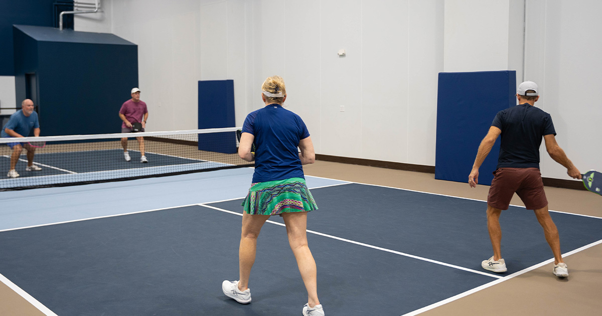 Four people playing doubles pickleball on a Tennis court.