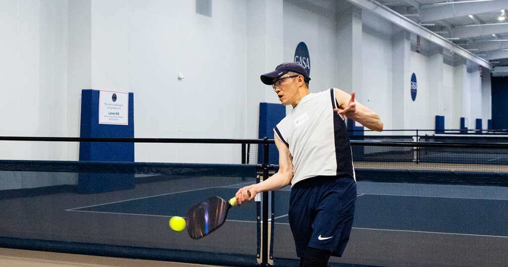 A singles pickleball player returns the ball on an indoor court, illustrating pickleball singles rules and gameplay.