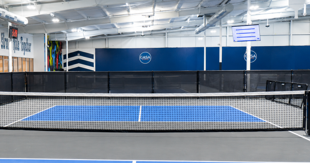 Indoor pickleball court with a black net and blue playing area.