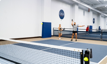 A man swings his paddle overhead to serve or smash a pickleball while his partner watches from across the net.