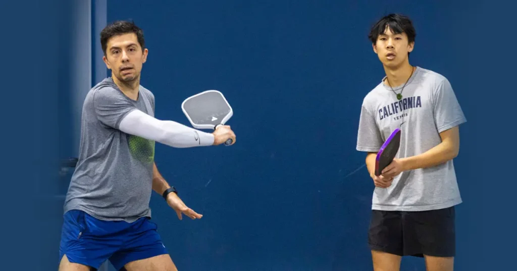 Two male players competing in an indoor pickleball game.