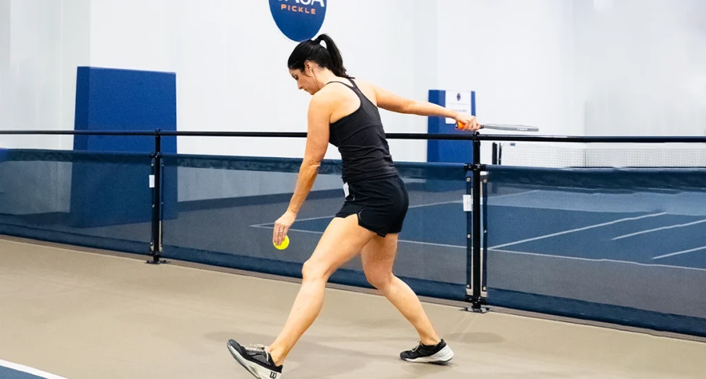 Woman serving at an indoor pickleball court.