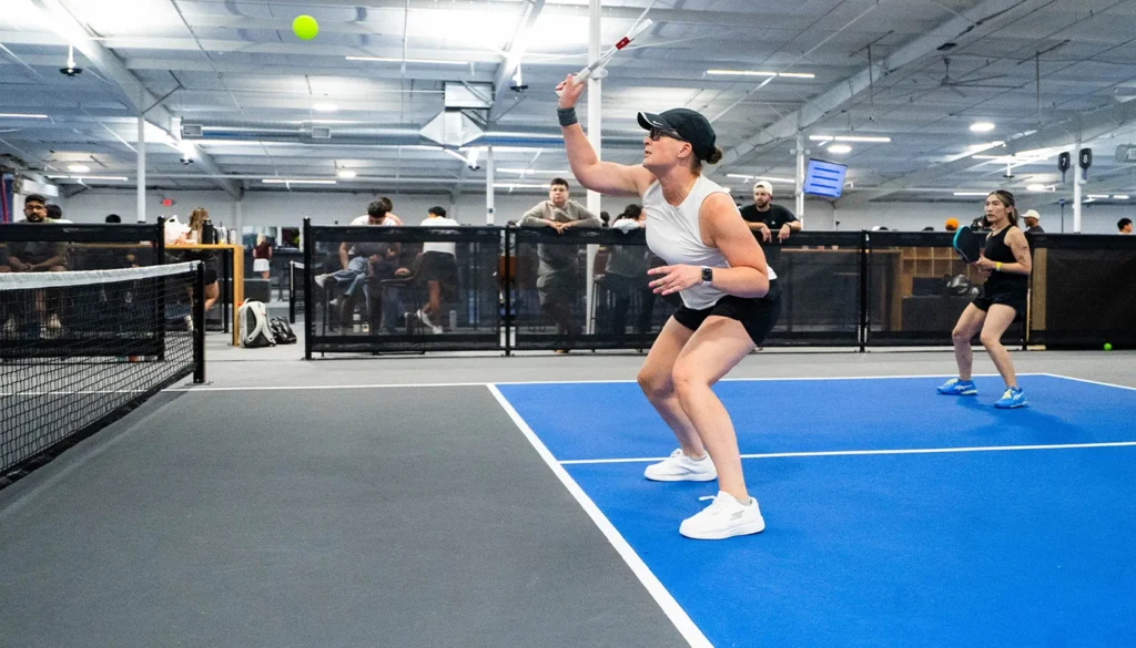 Woman in visor ready to hit pickleball on blue court.