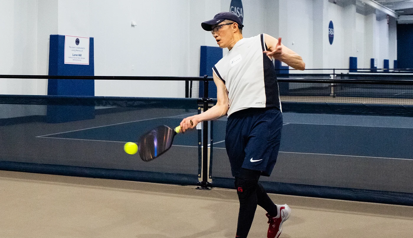 Man swinging paddle to hit yellow pickleball on indoor court.